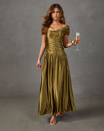 Woman in an olive green satin off-the-shoulder maxi dress with ruched bodice and flowy skirt, holding a champagne glass