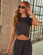 Woman wearing charcoal gray crop top and matching sweatpants set with black rectangle sunglasses, urban industrial backdrop