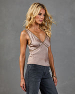 Woman wearing blush satin studded V-neck tank top with gold studs and gray high-waist jeans, fashion model pose