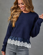 Navy blue knit sweater with white lace hem trim and satin underlay, styled with gray jeans on smiling woman