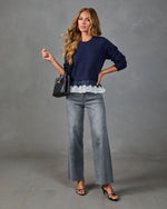 Woman wearing navy lace-trim sweater, wide-leg gray jeans, black strappy heels, holding woven black handbag