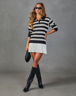 Woman wearing black and white striped polo sweater mini dress with pleated hem, knee-high black boots, and woven clutch