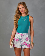 Woman wearing teal ribbed sleeveless top and white sequin floral shorts, styled with gold jewelry and cream clutch