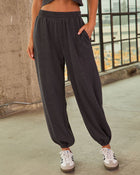 Charcoal gray women's oversized jogger sweatpants with elastic waistband and cuffs, paired with white Adidas Samba sneakers