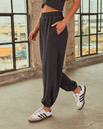 Charcoal gray women's fleece jogger sweatpants with elastic waist and cuffs, styled with white Adidas Samba sneakers
