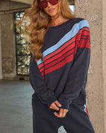 Navy blue colorblock sweatshirt with diagonal red and light blue stripes, worn with matching joggers and red sunglasses