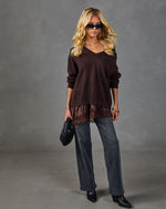 Woman wearing dark brown V-neck sweater with satin lace hem over gray wide-leg jeans, black ankle boots, and quilted clutch bag