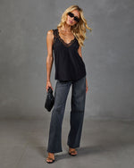 Black lace-trim satin cami top styled with gray wide-leg jeans, black heeled sandals, and woven clutch on blonde model