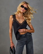 Black lace-trim satin cami top styled with gray high-waist jeans, gold jewelry, and dark sunglasses on blonde model
