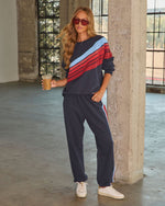 Woman wearing navy blue striped colorblock sweatsuit set with red and light blue stripes, white sneakers, red sunglasses, holding iced coffee