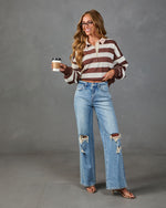 Woman wearing brown striped cropped rugby polo shirt, wide-leg distressed jeans, and strappy heels, holding coffee cup