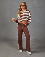 Woman wearing brown striped cropped rugby polo top and wide-leg brown track pants with white stripe, holding iced coffee