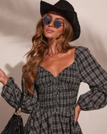 Woman in black plaid smocked dress, black woven cowboy hat, geometric sunglasses, holding fringe bag, western boho style