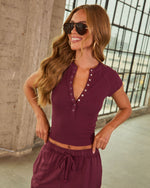 Woman wearing burgundy ribbed henley crop top with silver snap buttons and matching drawstring skirt, aviator sunglasses, urban setting