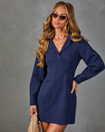 Navy blue long-sleeve mini blazer dress with V-neck collar, worn by a woman with wavy blonde hair and cat-eye sunglasses