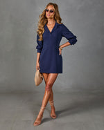 Navy blue long-sleeve mini blazer dress with V-neck collar, worn with nude strappy heels and woven clutch
