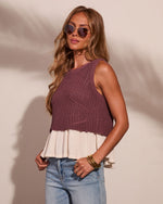 Woman wearing mauve knit sweater vest with cream pleated hem over light wash jeans, gold bangles, tinted aviator sunglasses