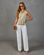 Woman wearing sage green sleeveless peplum top with white wide-leg jeans, strappy heels, and cognac crossbody bag
