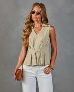 Woman wearing sage green sleeveless drawstring peplum blouse with white jeans, tan crossbody bag, and gold accessories