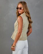 Woman wearing sage green sleeveless peplum top with side lace-up detail, white pants, gold bangles, and oval sunglasses