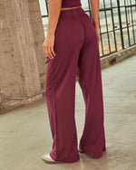 Women's burgundy wide-leg pants with elastic waistband, back view, worn with white sneakers in urban setting
