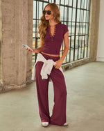 Woman wearing burgundy wide-leg pants and matching cropped henley top with gray hoodie tied around waist, aviator sunglasses