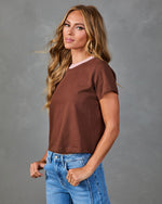 Woman wearing brown cropped short-sleeve tee with pink neckline detail and light wash high-waist jeans