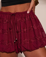 Burgundy ruffle mini shorts with lace trim, elastic drawstring waist, worn with black crop top and gold bangles