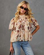 Floral print chiffon babydoll blouse in beige and brown, short flutter sleeves, mock neck, styled with blue jeans and sunglasses