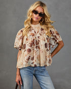 Floral print chiffon babydoll blouse in beige and brown, short flutter sleeves, mock neck, styled with blue jeans and sunglasses