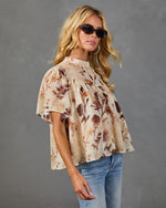 Woman wearing beige floral print babydoll blouse with flutter sleeves, paired with blue jeans and tortoise sunglasses