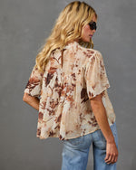 Woman wearing cream floral print babydoll blouse with flutter sleeves and keyhole back, paired with light wash jeans