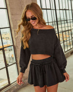 Woman wearing charcoal acid-wash off-shoulder crop sweatshirt and matching mini skirt set with black sunglasses
