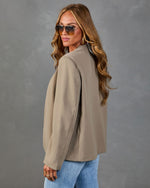 Woman modeling oversized taupe blazer jacket with blue jeans, aviator sunglasses, and wavy blonde hair, back view