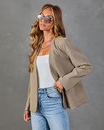 Woman wearing tan open-front blazer, white cami, blue jeans, and aviator sunglasses in fashion product photo