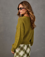 Olive green chunky knit sweater with cable sleeves, styled with a green and cream plaid midi skirt and sunglasses, back view
