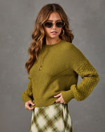 Olive green chunky knit sweater with cable sleeves, styled with a plaid midi skirt, gold hoop earrings and oval sunglasses