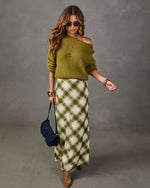 Woman in olive green off-shoulder knit sweater, plaid satin maxi skirt, suede ankle boots and navy shearling shoulder bag