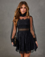 Black lace mini dress with sheer balloon sleeves, high mesh neckline, cutout waist and scalloped hem, styled with a clutch