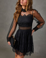 Black lace mini dress with sheer balloon sleeves, mock neck, cutout waist and scalloped hem, styled with a black clutch