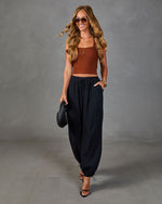 Woman wearing rust ribbed crop top and black linen harem pants with strappy heels and woven clutch, boho chic style