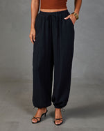 Black wide-leg drawstring jogger pants with textured fabric, elastic ankles, and side pockets, styled with a rust crop top