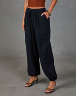 Black textured drawstring jogger pants with elastic ankles, paired with rust crop top and black strappy heels