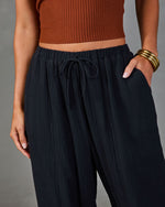 Woman wearing navy blue textured wide-leg drawstring pants with elastic waist and rust ribbed crop top, gold bangles