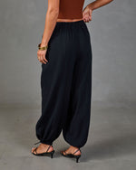 Black harem pants with elastic waist and ankles, styled with rust crop top and strappy kitten heels, rear view