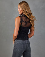 Woman wearing black floral lace sleeveless bodysuit with sheer back panel, paired with gray skinny jeans, back view