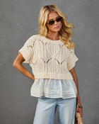 Woman wearing cream cable-knit crop sweater with chiffon peplum hem over light wash jeans, styled with tortoise sunglasses