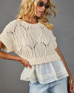 Cream cable knit crop sweater with open-weave pattern layered over white ruffle hem top and light wash jeans