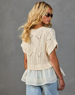 Women's cream cable-knit short-sleeve sweater with ruffled hem layered over white blouse, styled with light-wash jeans