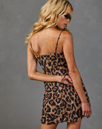 Woman wearing leopard print mini slip dress with spaghetti straps, open back, viewed from behind, styled with gold bangles and sunglasses